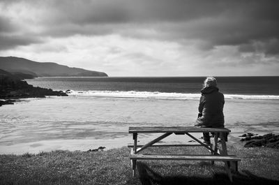 Rear view of woman sitting on picnic table at beach