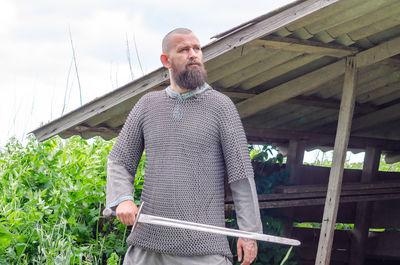 Sword in hands of medieval viking warrior on background of old wooden building. militant look.