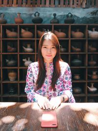 Portrait of young woman sitting against shelves