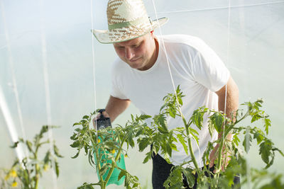 Midsection of man holding hat while standing against plants