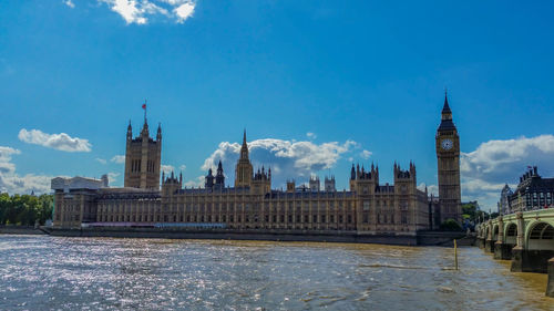 Palace of westminster and big ben by thames river against blue sky