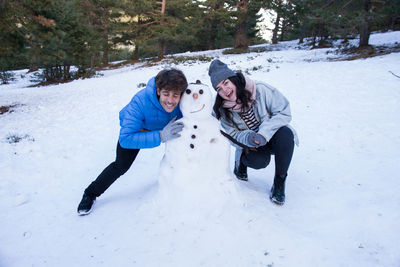 Portrait of young couple with snowman during winter