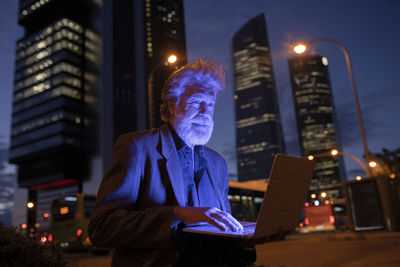 Male professional using laptop in city at night