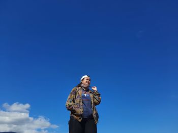 Low angle view of woman holding smart phone against blue sky