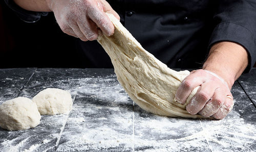 Midsection of chef kneading dough on table