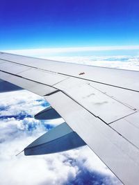 Cropped image of airplane flying over clouds against blue sky