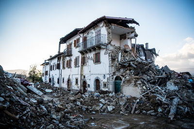 Abandoned house by building against sky