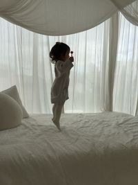 Side view of girl jumping on bed holding candy at home
