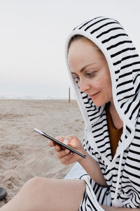 Side view of woman using smart phone sitting at beach