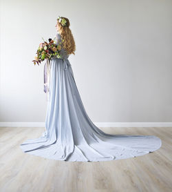 Woman wearing dress holding bouquet against white wall