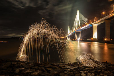 Light trails in illuminated city against sky at night