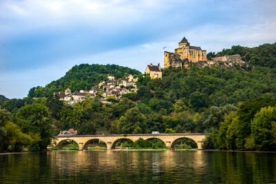 Arch bridge over river by buildings against sky