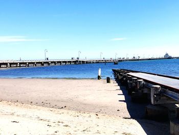 Pier on beach against blue sky