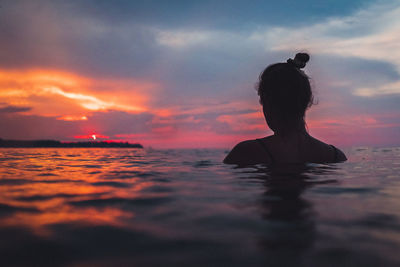 Silhouette woman in sea against sky during sunset