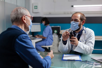 Doctor wearing mask showing medicine to patient