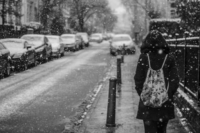 Rear view of woman walking on sidewalk in city during snowfall