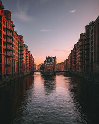 Canal amidst buildings in city during sunset