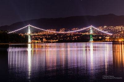 Illuminated bridge over river against sky at night