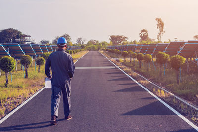 Rear view of electrician walking on road amidst solar panels