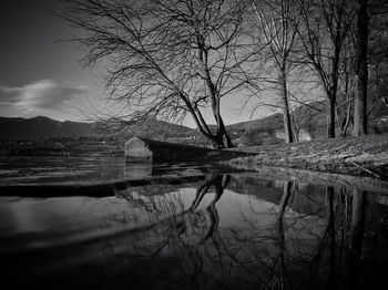 Reflection of bare trees in lake against sky