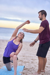 Fitness instructor assisting woman in exercising at beach