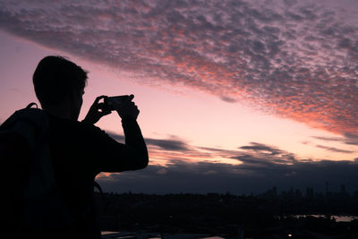 Silhouette man photographing cityscape against sky during sunset