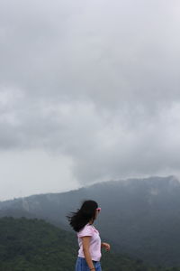 Side view of woman standing on mountain against sky