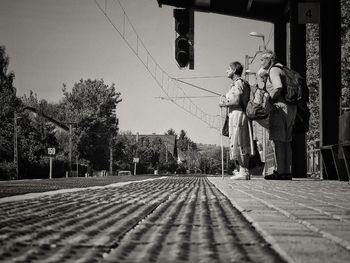 People standing by railroad tracks in city against sky