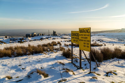 Yellow warning signs on snow covered field against sky