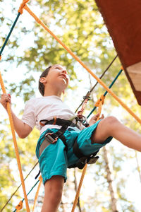 Low angle view of boy on obstacle course in forest