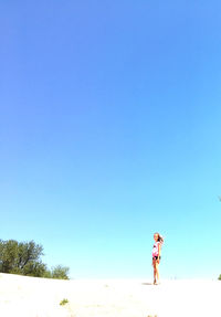 Girl standing at beach against clear blue sky