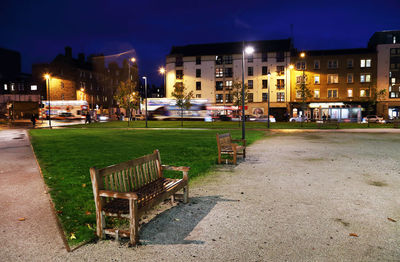 Empty wooden benches by grass in city at night