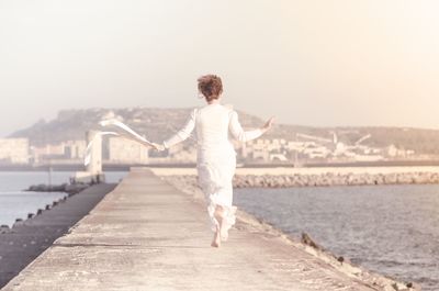 Rear view of woman levitating over promenade against clear sky