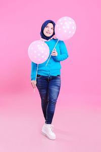 Woman holding balloons against pink background