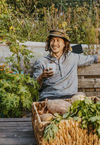 Smiling male farmer with coffee cup sitting on bench at farm