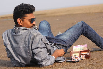 Young man sitting by purse and phone at beach