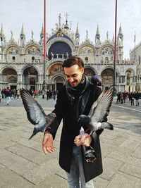 Smiling man feeding birds while standing on street