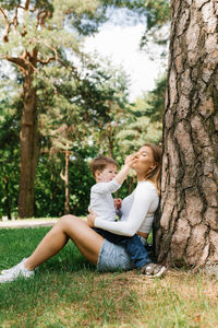 Cute boy sitting with mom on the grass and having fun together