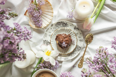 Top view of antique tableware, chocolate profiterole and decor of lilac and tulip flowers in bed.