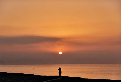Silhouette person standing on sea against sky during sunrise