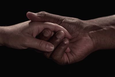 Close-up of couple holding hands over black background