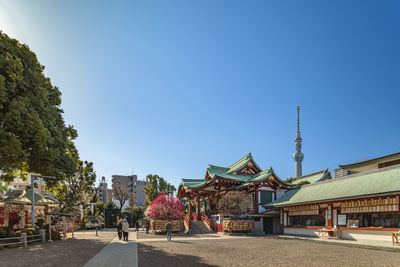 People by buildings against clear blue sky