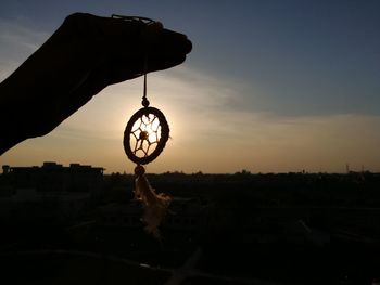 Close-up of silhouette hand hanging against sky at sunset