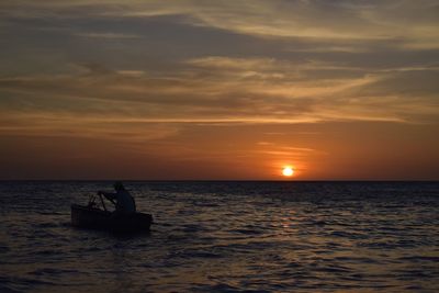 Silhouette man in sea against sky during sunset