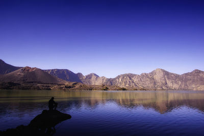 Scenic view of lake and mountains against clear blue sky