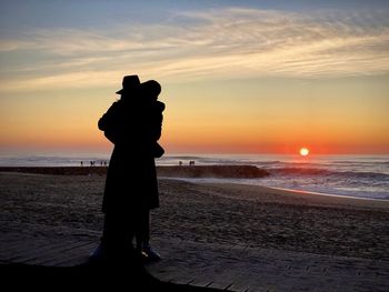 Silhouette couple standing at beach against sky during sunset