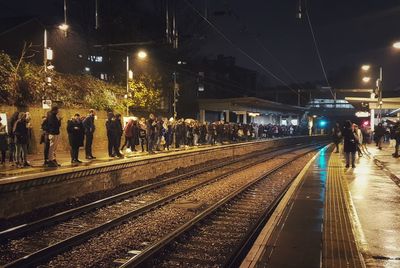 People waiting at railroad station platform at night