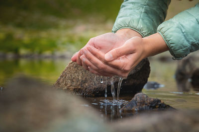 Close-up of water drops falling from female hands into a stream. the hand touches fresh water. a