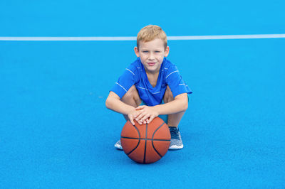 Portrait of boy holding basketball while crouching on court