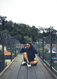 Man sitting on footbridge against sky